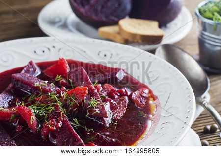 Vegetable soup - red borsch in a white bowl on a rustic wooden background clouse up. Healthy beetroot soup vegetarian food. Delicious beet soup with croutons.