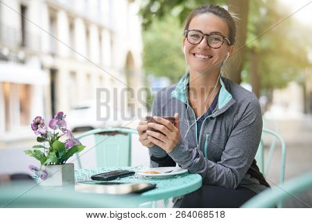  Woman sitting outisde of a coffee shop with headphones and devices                              