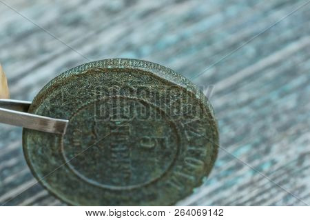 Tweezers Holding Old Copper Green Coin On The Table