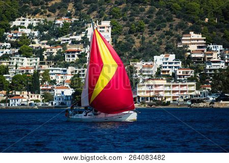 Sailing yacht under red gennaker goes along the Greek coast, the Aegean sea.
