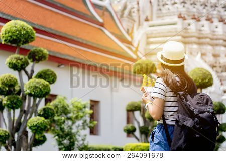 Title: Tourist Women With Carrying A Backpack Viewing Poster, About The Temple In Bangkok At Arunrat