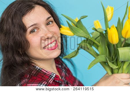 Close-up Portrait Of Beautiful Young Woman With Yellow Tulips On Blue Background