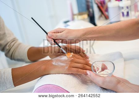 Close-up Of Beautician Applying Cream On Woman's Hand Using Brush.