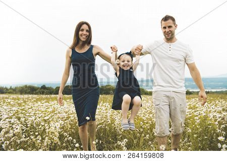 Parent Walking With Her Baby Son On Daisy Field At The Sunset Time