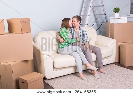 Moving And Real Estate Concept - Happy Couple Kissing On Sofa In Their New Flat