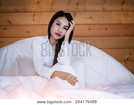 The beautifu laday is sitting on bed,put her hand touch head,unhappy feeling,headache from tried and