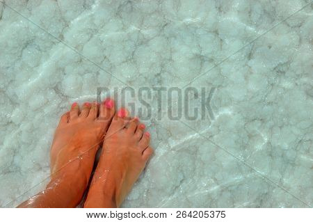 Female Feet With Manicure On Stone, Covered With Salt Formations Between The Waves In The Water. Cry