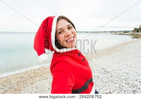Christmas, Humor And People Concept - Young Woman In Santa Suit Making Selfie Near The Sea At Summer