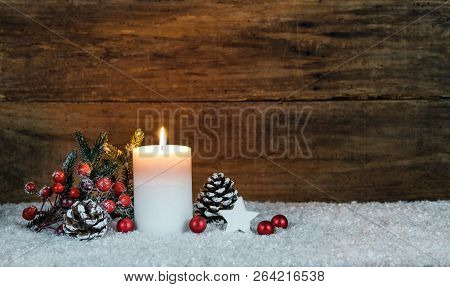Burning Advent Or Christmas Candle With Fir Tree Branch, Red Berries, Pine Cones And Ornaments On Sn