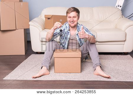 New Home, Real Estate Owner And Moving Concept - Young Man Holding Keys Of New Home And Showing Thum