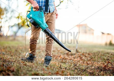 Gardener Clearing Up Leaves Using An Electric Leaf Blower Tool. Gardening Details