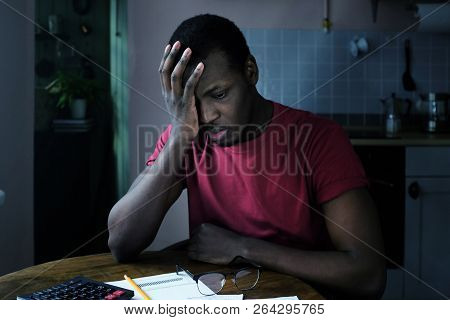 Young Frustrated African American Man With Financial Troubles, Sitting At Kitchen Table With Papers,