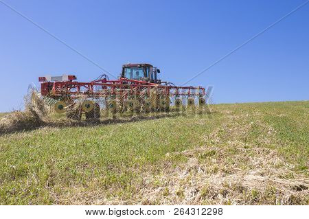 Tractor Raking Hay Over Sloped Ground. Heavy Wire Spokes Wheels Made Are Pulled By A Tractor For Gat
