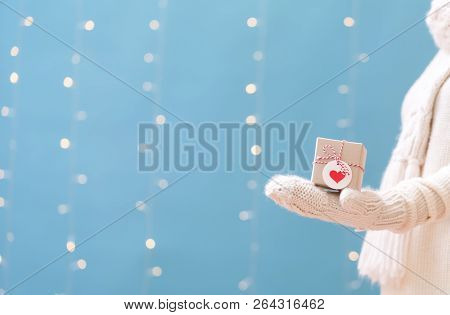 Woman Holding A Christmas Gift Box On A Shiny Light Blue Background