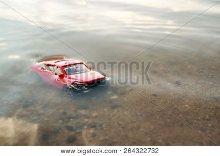 Red Toy Car Submerged In The Water, Drowned In The Pond Facing Us, The Accident In The Summer On The
