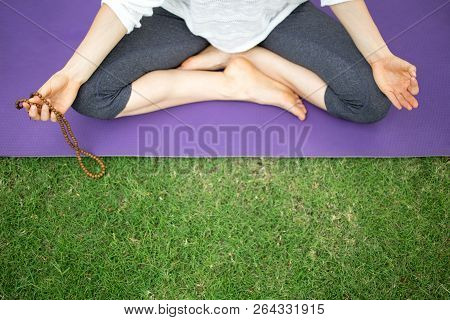 Top View Of Young Caucasian Woman Sitting Barefoot On Mat, Holding Rosary Beads And Meditating Outdo