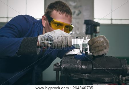 Man Worker Is Working With Iron Detail On Vise Grip On Blacksmith Table And Is Measuring A Diameter 