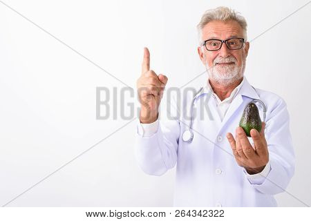 Studio Shot Of Handsome Senior Bearded Man Doctor Holding Avocad