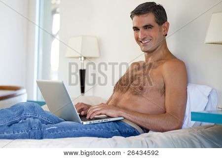Portrait of smiling shirtless middle aged man working on laptop