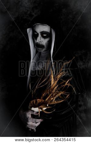 portrait of a frightening evil nun, wearing a typical black and white habit, with a dry bouquet of flowers in her hands