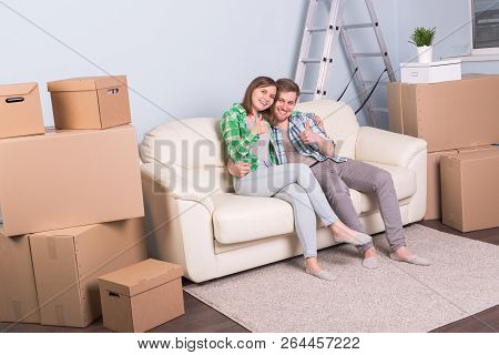 Moving And Real Estate Concept - Happy Couple Kissing On Sofa In Their New Flat