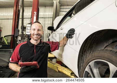 Handsome Mechanic Based On Car In Auto Repair Shop With Tablet On Hand
