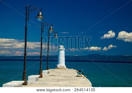 White Pier Jetty With Bench, Lampposts And Lighthouse On Blue Paradise Water Of Toroneos Kolpos Gulf