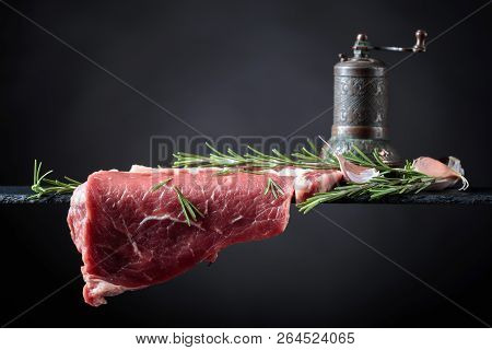 Raw Beef Steak With Peppermill, Garlic And Rosemary. Black Background, Copy Space.