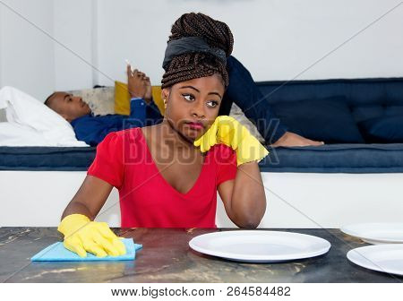 Frustrated African American Woman Cleaning Room With Lazy Man At Home At Flat