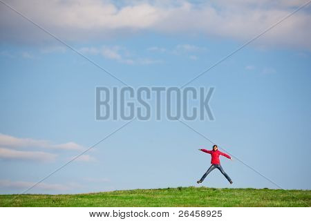 joyful young woman jumping in the middlle of a green field