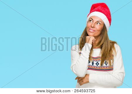 Middle age adult woman wearing winter sweater and chrismat hat over isolated background with hand on chin thinking about question, pensive expression. Smiling with thoughtful face. Doubt concept.