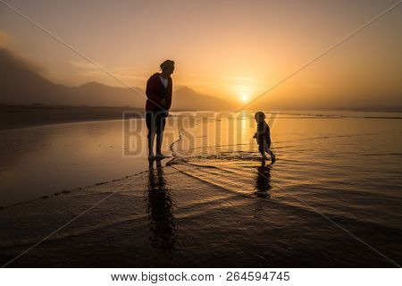 Silhouette of young mother son walking on reflected beach in Cofete, Fuerteventura, Canary Islands, Spain.