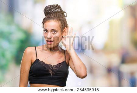Young braided hair african american with pigmentation blemish birth mark over isolated background smiling with hand over ear listening an hearing to rumor or gossip. Deafness concept.