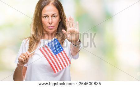 Middle age hispanic woman holding flag of United States of America over isolated background with open hand doing stop sign with serious and confident expression, defense gesture