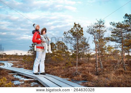 Young Mother With Her Little Daughter In A Baby Carrier Outside Walking On Trail In Swamp, Kemeri Na