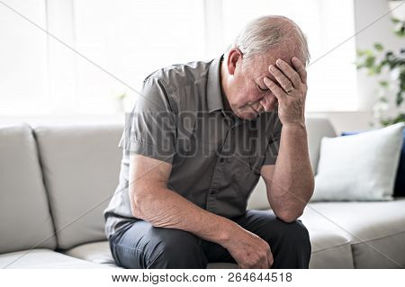 Senior Man Thinking And Sitting On Sofa At Home Like Sad