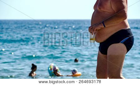 Fat Guy On The Beach  With A Glass Of Beer. Big Belly Enjoying Sun At The Beach. Concept Of All Incl