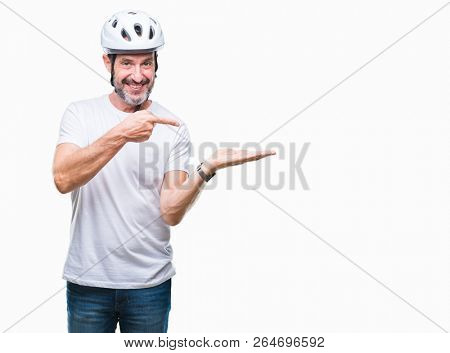 Middle age senior hoary cyclist man wearing bike safety helment isolated background amazed and smiling to the camera while presenting with hand and pointing with finger.