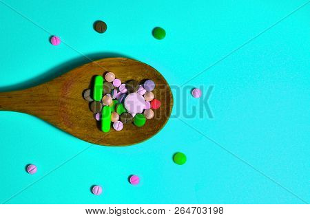 Assorted Pharmaceutical Medicine Pills, Tablets And Capsules On Wooden Spoon. Blue Background