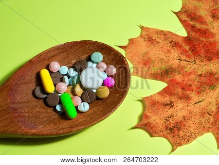 Assorted Pharmaceutical Medicine Pills, Tablets And Capsules On Wooden Spoon. On A Green Background