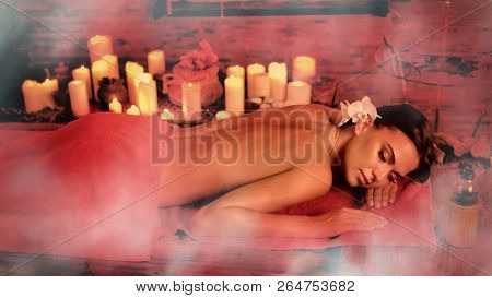 Massage Filipino of woman in spa salon. Girl on candles aglow background in steam room. Luxary ayurveda interior in oriental therapy salon. Photo effect with red toning. Artistic effect of steam