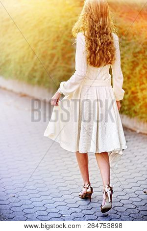 Fashion woman in autumn spring dress on city street . Back of female style of feminine fashionable girl model wallking cobblestone pavement outdoor. Color tone on shiny sunlight background.