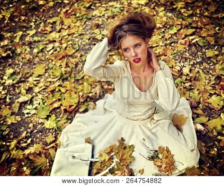 Autumn fashion feminity lace dress with long sleeve below knee in princess style. Top view of woman dramatic look sitting on fall leaves in city park outdoor.