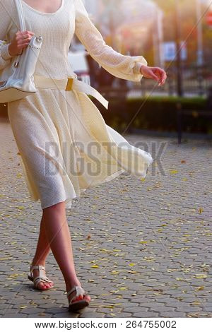 Fashion woman in autumn-spring dress on city street. Cropped shot of female style of feminine fashionable girl model wallking low heel fall outdoor. Color tone on shiny sunlight background.