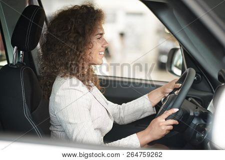 Beautiful Woman With Curly Hair Sitting In Car Cabin And Testing. Female Customer Smiling And Holdin