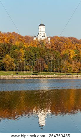 Colorful autumn. Alley along the riverbank on the background of the autumn park. Reflections in the