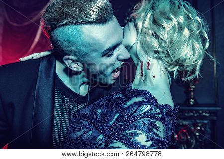A beautiful couple of vampires in a dark room. Bite of a vampire. Classic style. Beauty, fashion.