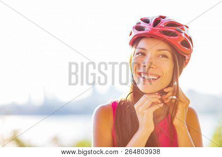 Cyclist woman putting bike helmet on - head protection on outdoor sport activiy or commute lifestyle in city. Asian girl on bicycle during summer.