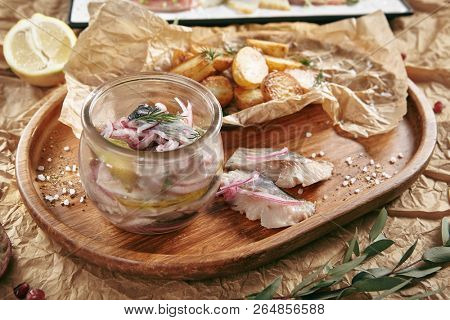 Marinated Herring in Vinegar with Potatoes, Oil, Dill, Onion and Spices on Rustic Background. Beautiful Creative Sea Food Vintage Design of Pickled Fish Fillet with Baked Potato on a Wooden Tray