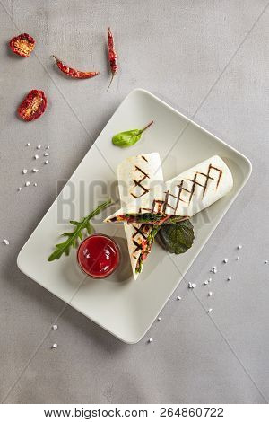 Barbeque Meat Shaverma or Doner Kebab with Vegetables on White Plate. Thin Tortilla Rolls Stuffed with Sliced Fried Beef, Pork and Chicken Fillet Cucumber, Tomato, Sauce, Paprika and Greens